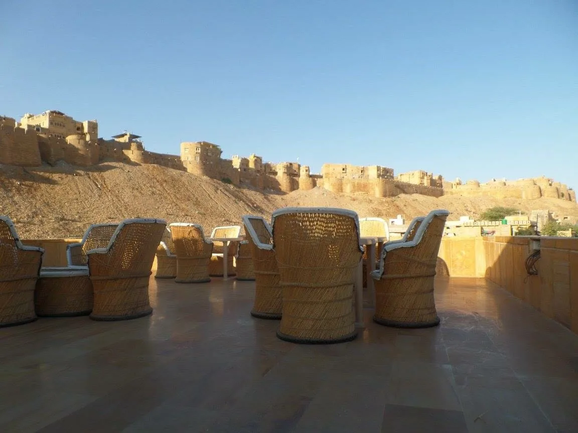 The rooftop terrace at Mamamia Jaisalmer, cane chairs facing the walls of Jaisalmer Fort in late afternoon light
